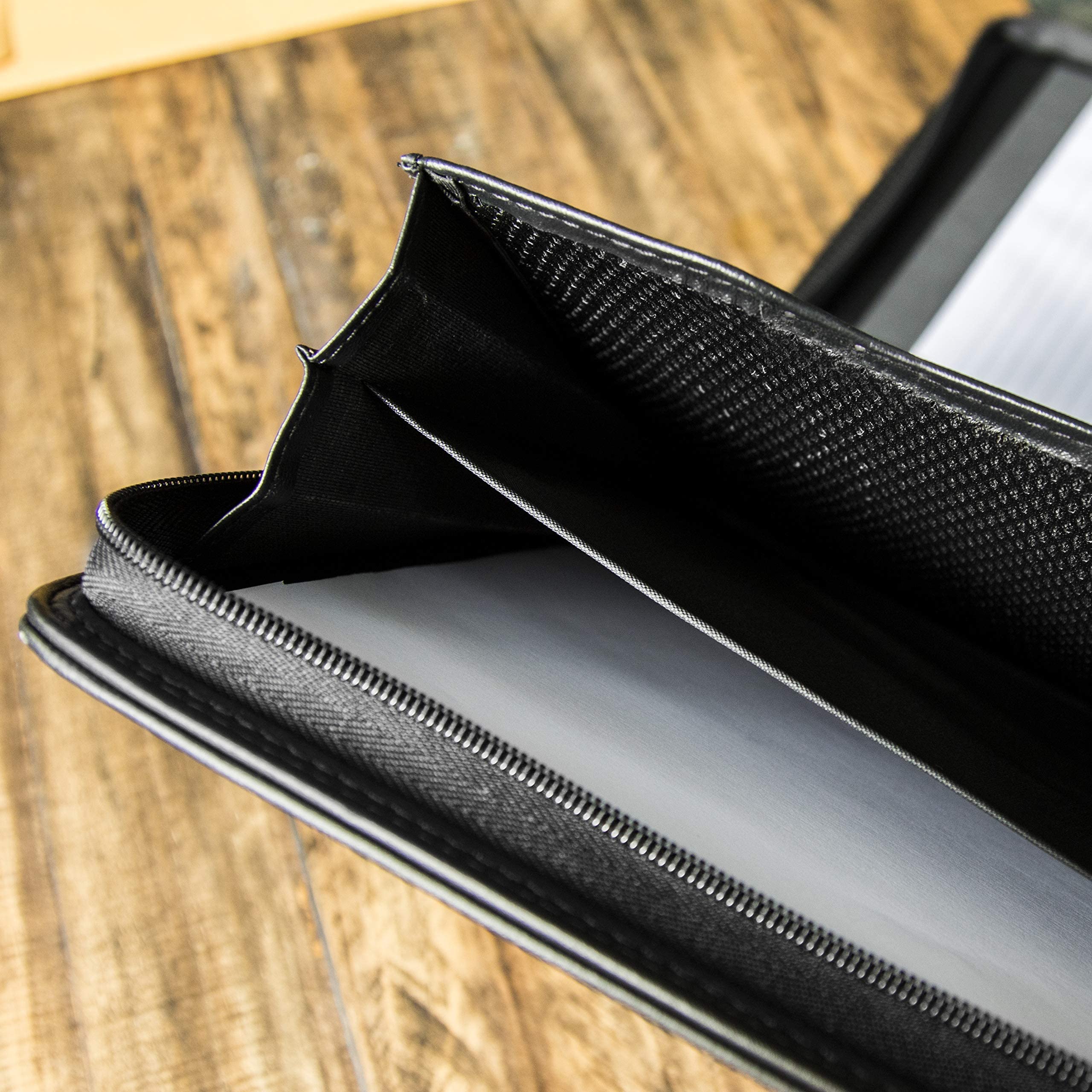  A professional black vegan leather Cossini business portfolio zipped shut, paired with a smartphone and a silver pen on a sleek dark surface. Features the Bold Leadership Path logo